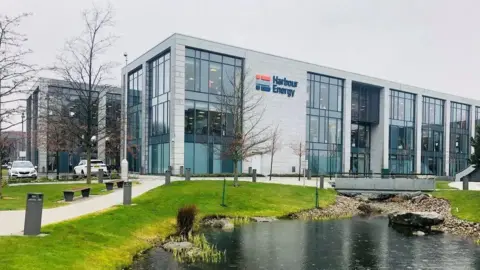 Harbour Energy building, with cars parked next to it, and a pond in the foreground.