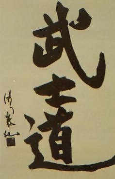 Large Black characters in Asian script on a gray-yellow piece of paper.