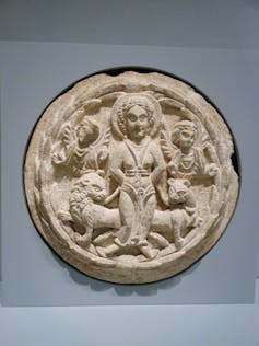 A circular stone with carvings of a bound woman flanked by two lions.