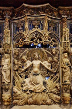 An ornate carving depicts a woman, stripped to the waist, who holds out her arms as she seems to stand atop flames.