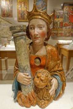 A small statue shows a woman wearing a crown as she puts one arm around a pillar and the other around a lion.