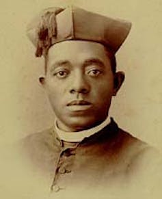A sepia-toned portrait of a Black man wearing a clerical hat, white collar and buttoned-up jacket.