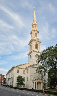 A white church with a tall steeple rising into a blue sky with wispy clouds.
