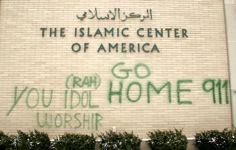 A beige wall that says The Islamic Center of America has graffiti on it that says 'Go Home 911' and 'You Idol Worship'